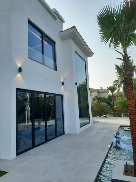 Glazing across a villa exterior: Dark-framed doors and windows alongside a tall glazed opening overlooking the terrace.